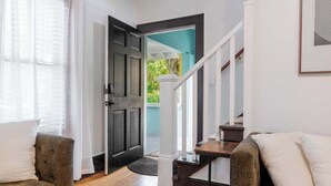 A modern living room with a wooden floor, a dark door, and a staircase leading to a balcony. - Sanctuary on 3rd | Walk to UF • Parking • Grill (Gainesville)