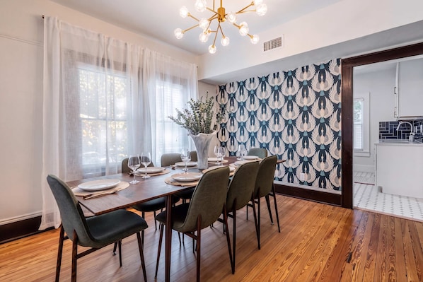 Un comedor con una mesa de madera dispuesta para seis personas, una araña y un papel tapiz estampado.