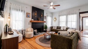 A living room with a fireplace, a ceiling fan, and a sofa. - Sanctuary on 3rd | Walk to UF • Parking • Grill (Gainesville)