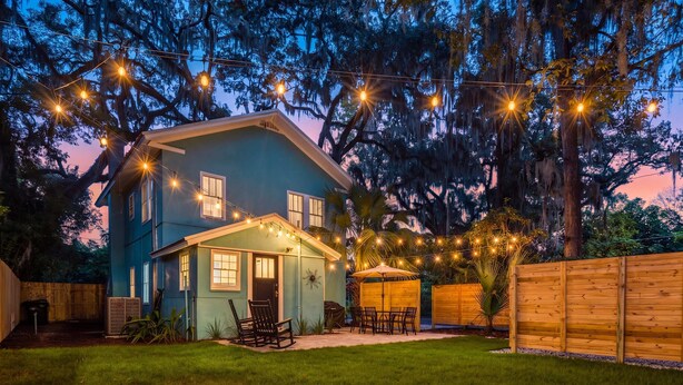 A two-story house with a covered patio, string lights, and a wooden fence. - Sanctuary on 3rd | Walk to UF • Parking • Grill (Gainesville)