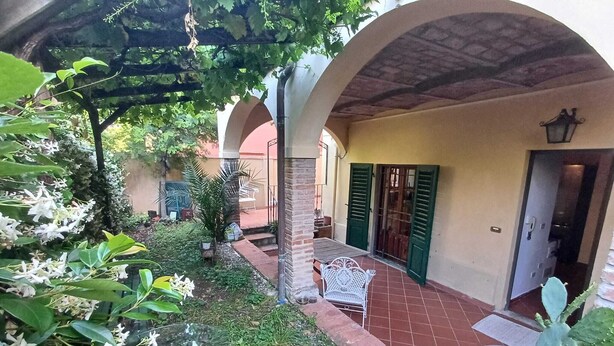 Un patio con una pérgola, un banco de metal blanco y una planta de cactus.