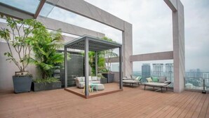 A modern rooftop terrace with a glass enclosure, seating area, and potted plants. - Riveria City near KL Sentral with Sky Infinity Pool by COBNB (Kuala Lumpur)