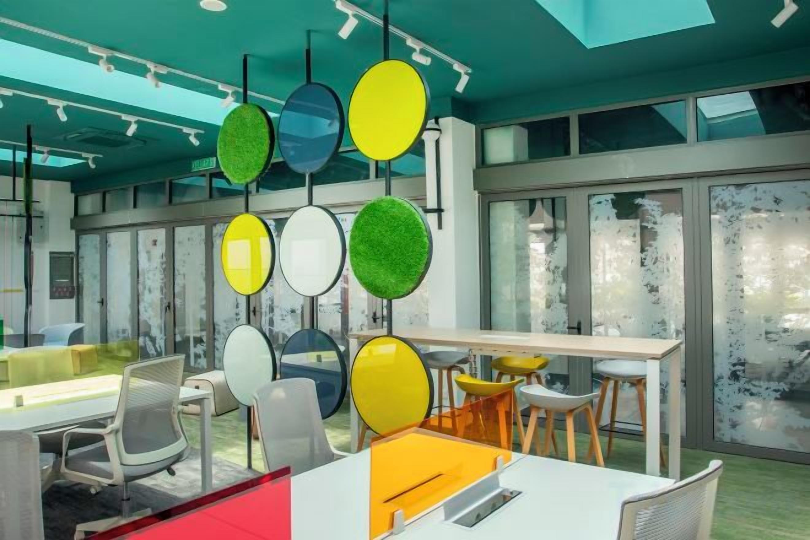 Un espacio de oficina con varios puestos de trabajo, una mesa larga y un gran ventanal que proporciona luz natural.