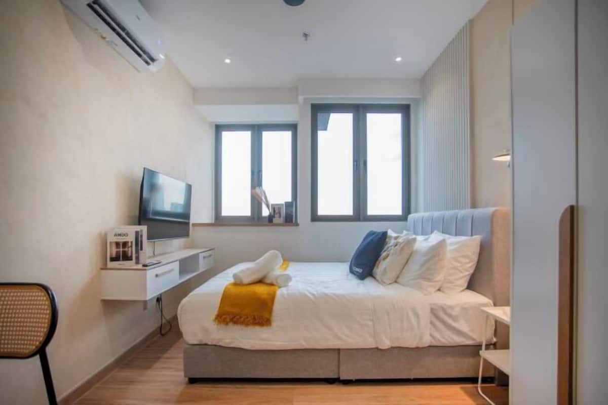 A modern bedroom with a bed, a TV, a desk, and large windows.
