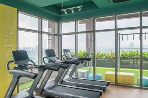 A gym with treadmills, a yellow wall with "WORK TO" text, large windows, and a view of greenery and buildings. - Riveria City near KL Sentral with Sky Infinity Pool by COBNB (Kuala Lumpur)