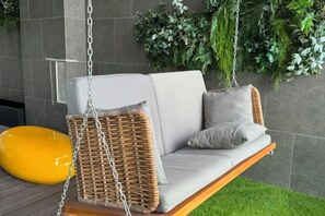 A wicker swing chair with cushions, a yellow bean bag, and green plants in a modern indoor setting. - Riveria City near KL Sentral with Sky Infinity Pool by COBNB (Kuala Lumpur)