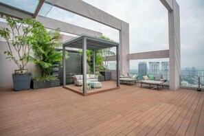 A rooftop terrace with a glass enclosure, seating area, and potted plants. - Riveria City near KL Sentral with Sky Infinity Pool by COBNB (Kuala Lumpur)