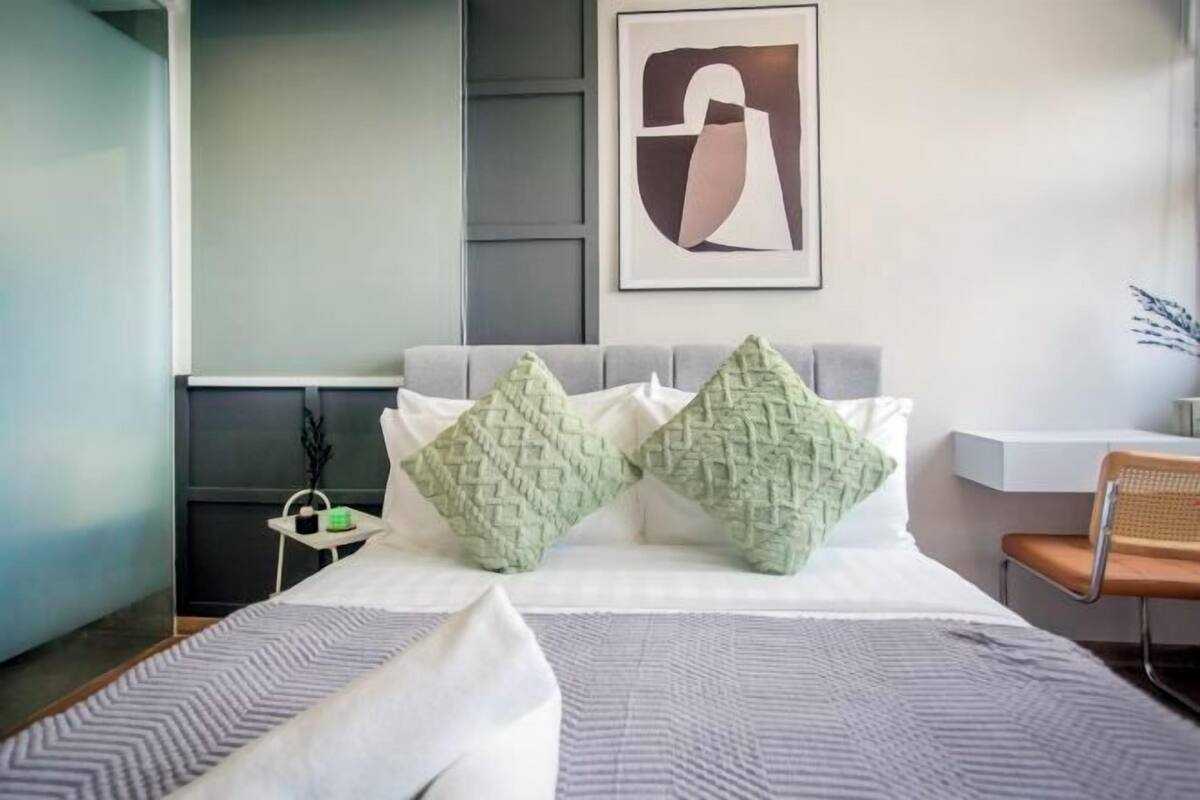 A modern hotel room with a bed, pillows, a chair, and a framed artwork on the wall.