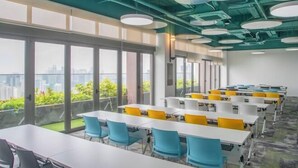 A modern conference room with large windows, white tables, and blue and yellow chairs. - Riveria City near KL Sentral with Sky Infinity Pool by COBNB (Kuala Lumpur)