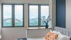 A bedroom with a bed, a window with a city view, a ceiling fan, and a potted plant. - Riveria City near KL Sentral with Sky Infinity Pool by COBNB (Kuala Lumpur)