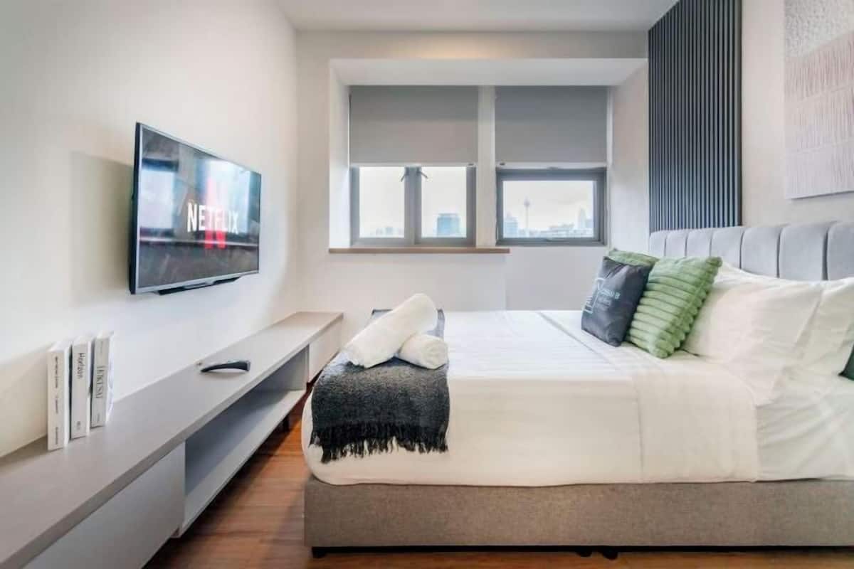 A modern bedroom with a bed, a TV, a window, and a bedside table.