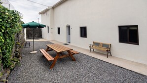 Un patio con una mesa de picnic de madera, un banco y una sombrilla verde.