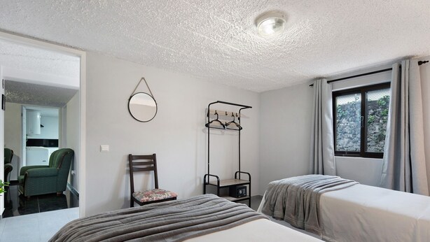 Un dormitorio con dos camas, una silla, perchero y una ventana con cortinas.