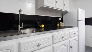 Una cocina con armarios blancos, un lavamanos de acero inoxidable y un refrigerador blanco.