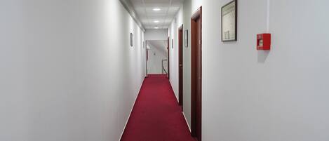 A long, narrow hallway with white walls and a red carpet, leading to a door at the end.