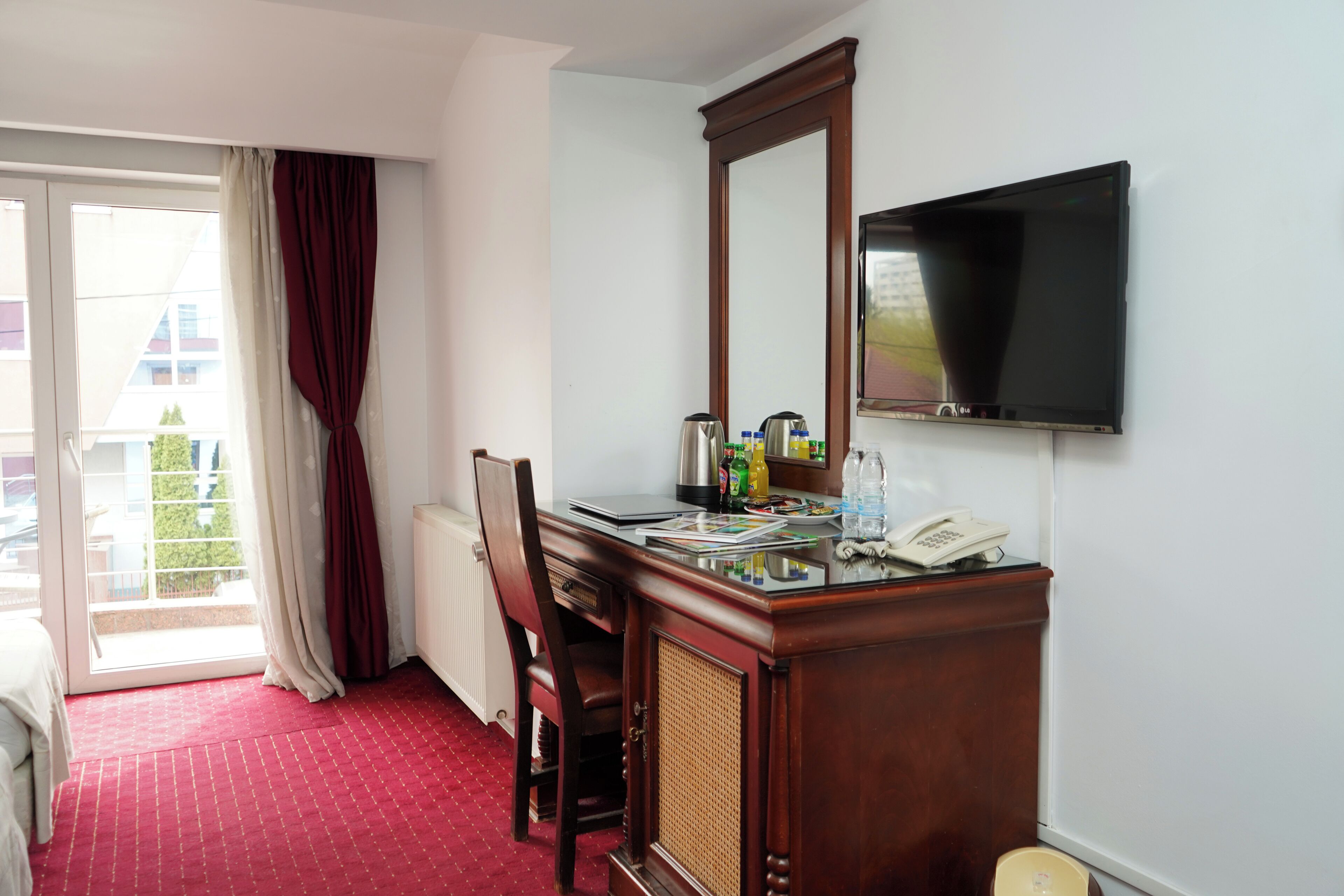 Une chambre d’hôtel avec un lit, un bureau avec un téléphone, une machine à café et un téléviseur fixé au mur.