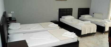 A hotel room with three beds, a painting on the wall, and a radiator.