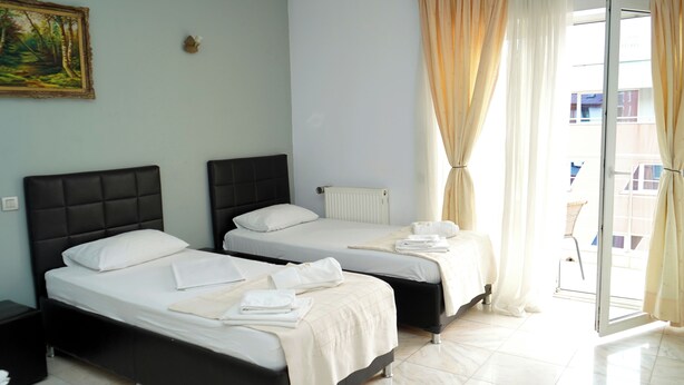 A hotel room with two beds, a radiator, a painting on the wall, and a view through a window with curtains.