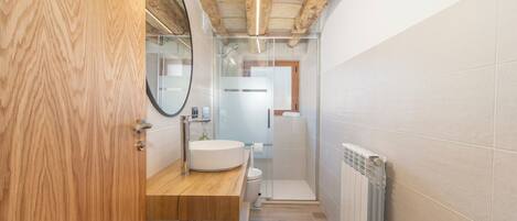 A bathroom with a wooden vanity, a round mirror, a toilet, and a shower enclosure.