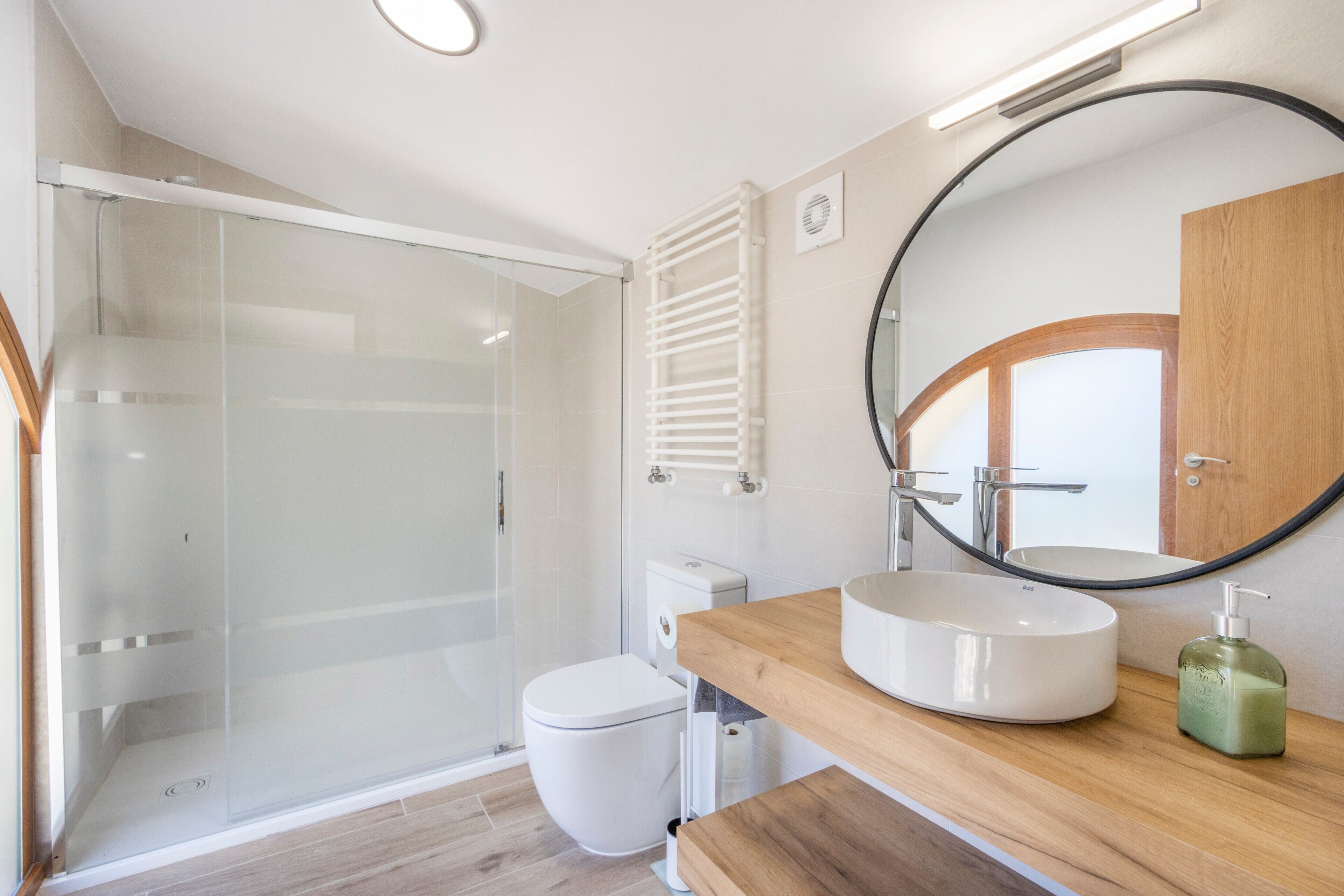A modern bathroom with a glass shower enclosure, a toilet, a sink with a wooden countertop, and a mirror with a wooden frame.