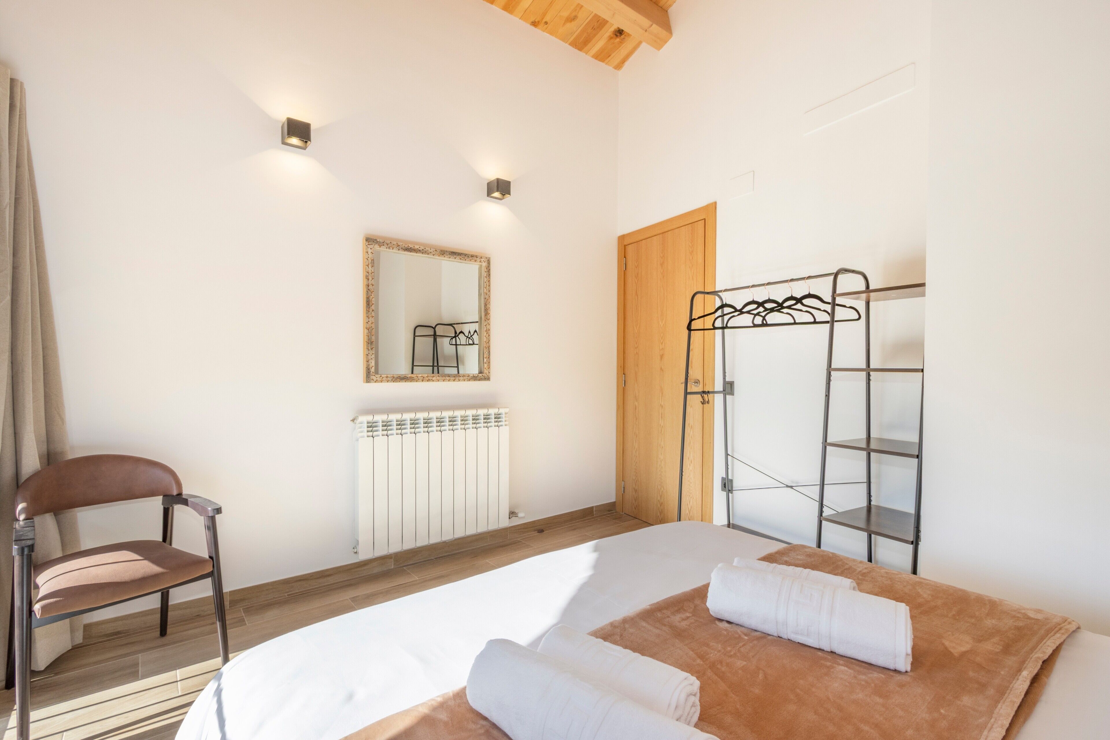 A bedroom with a bed, a chair, a wooden door, a radiator, and a mirror.