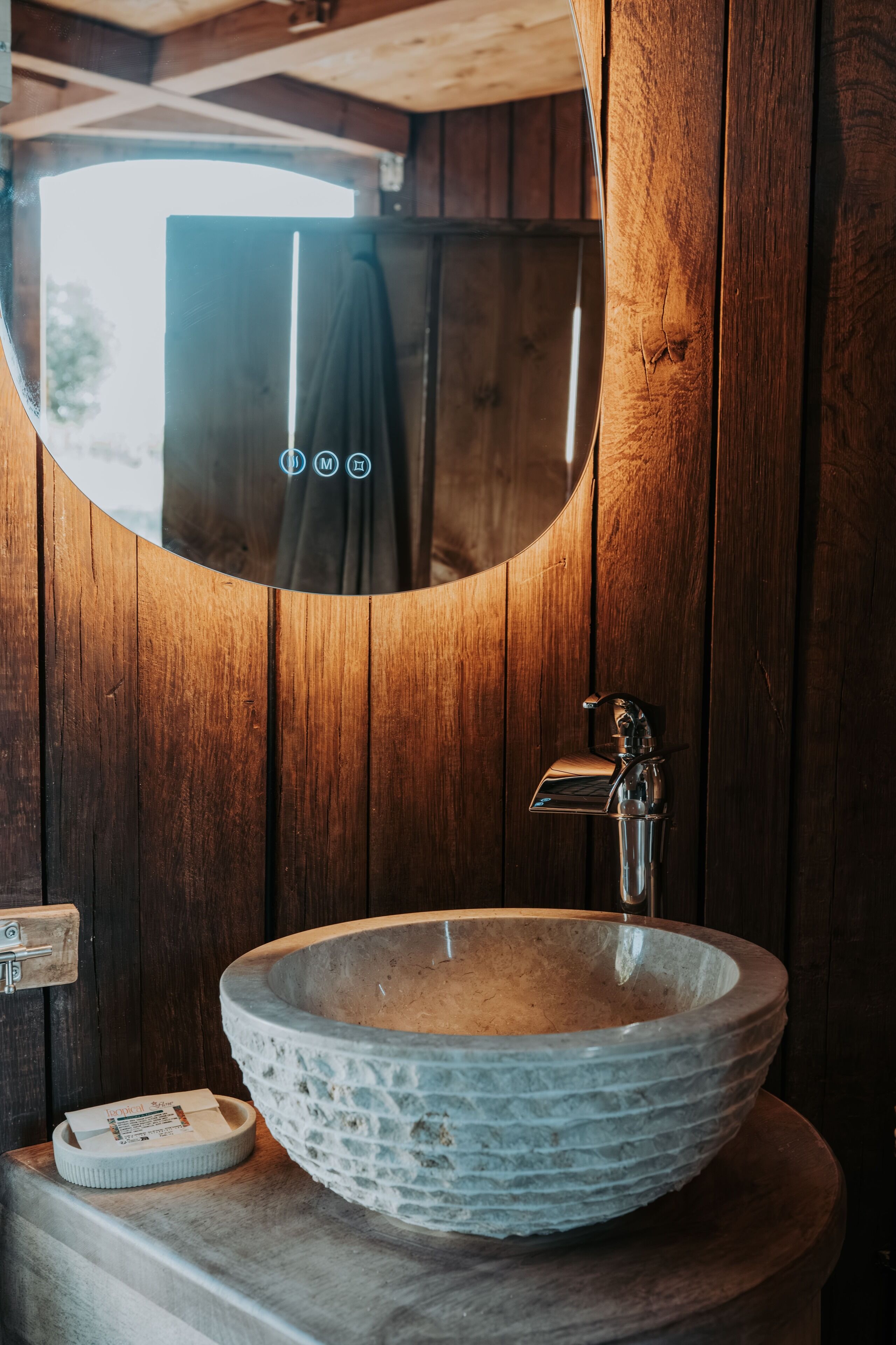 A rustic bathroom with a wooden wall, a round stone sink, and a mirror.