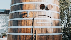 A large wooden barrel-shaped structure with a door and two circular windows, surrounded by trees. - Le Nid du Coucou (Cocumont)