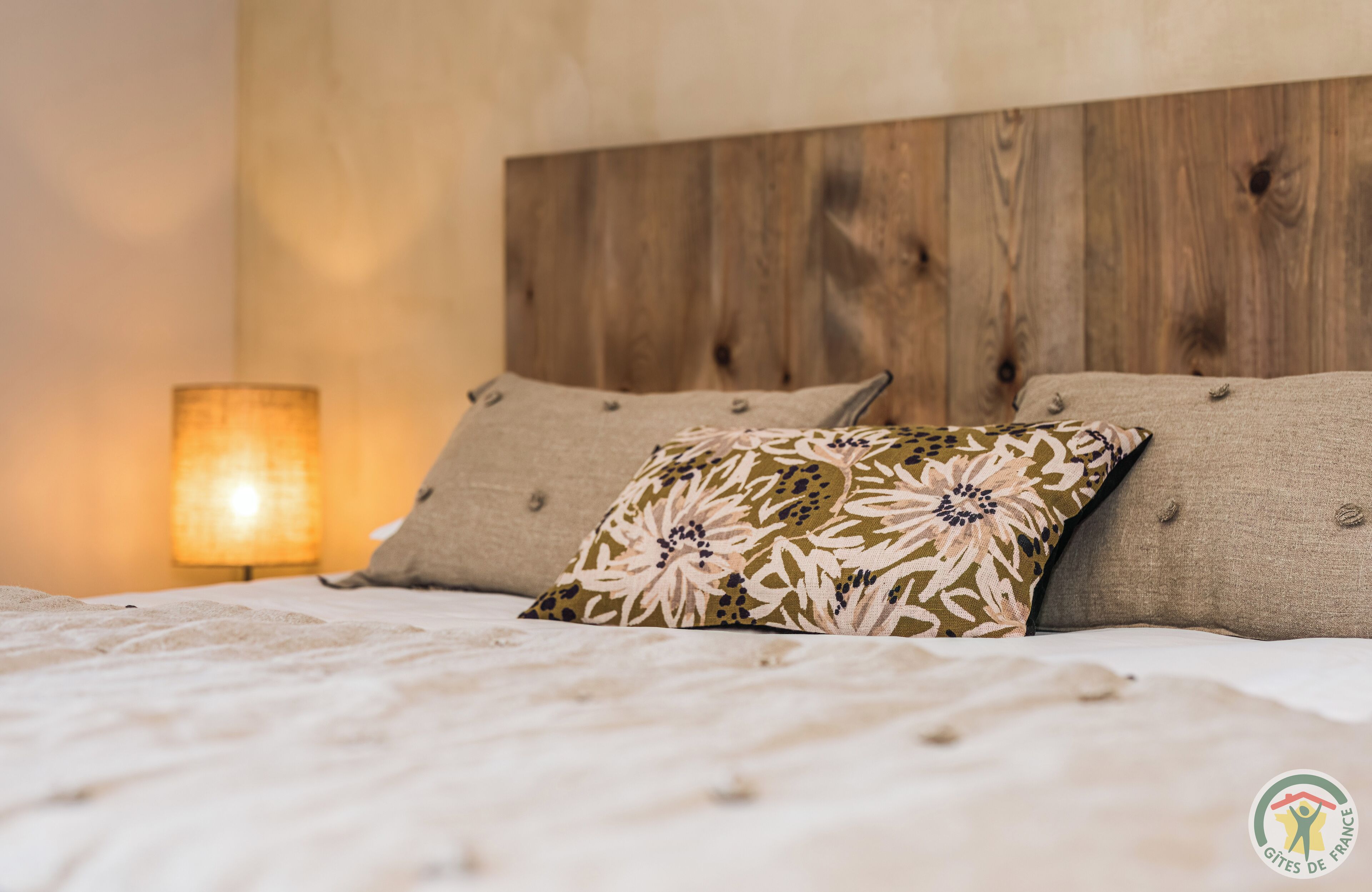 A bed with a wooden headboard, a lamp, and a floral pillow.