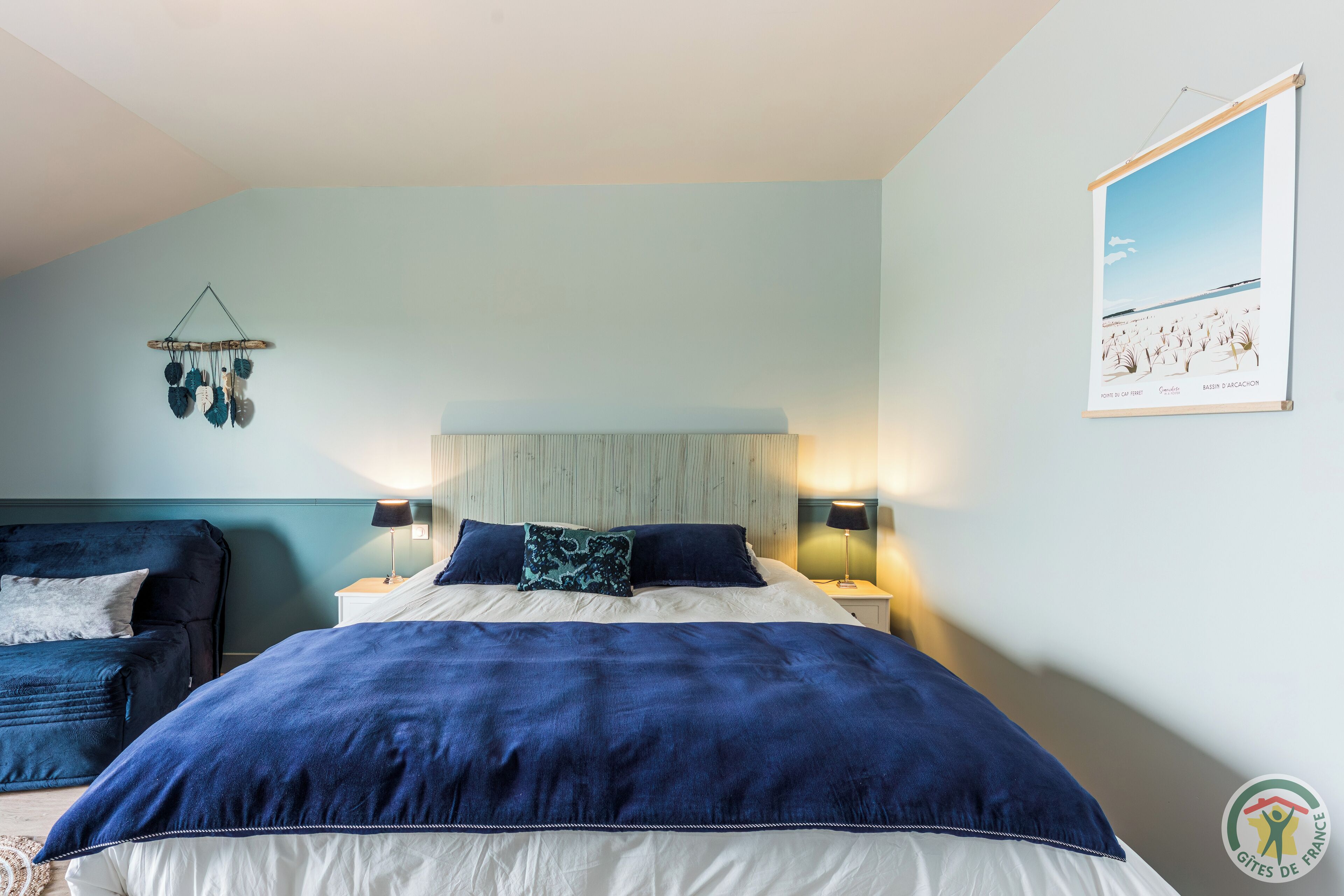 A bedroom with a large bed, two bedside tables, a hanging light fixture, and a poster on the wall.