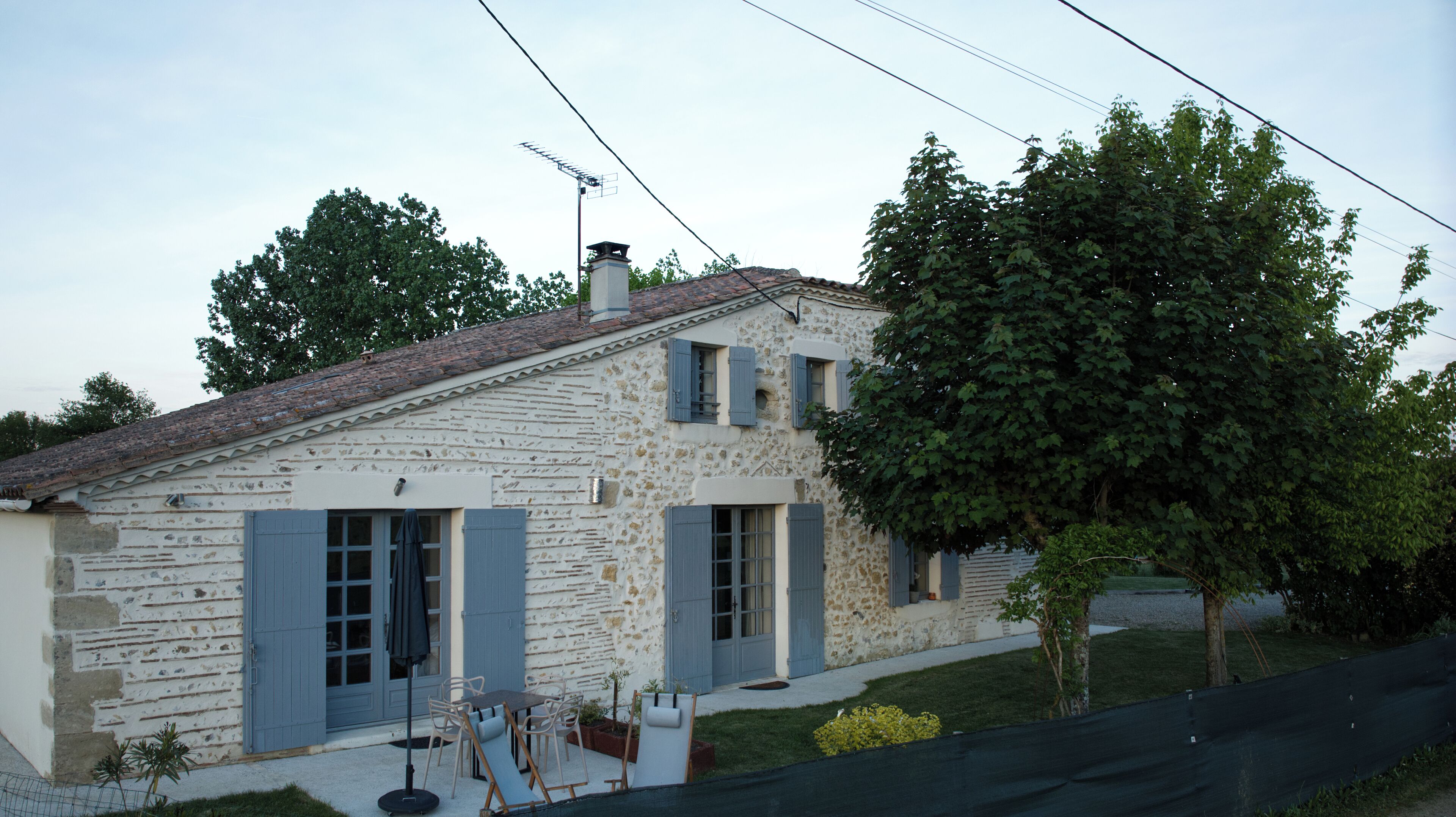 A stone house with blue shutters, a tiled roof, and a small garden.