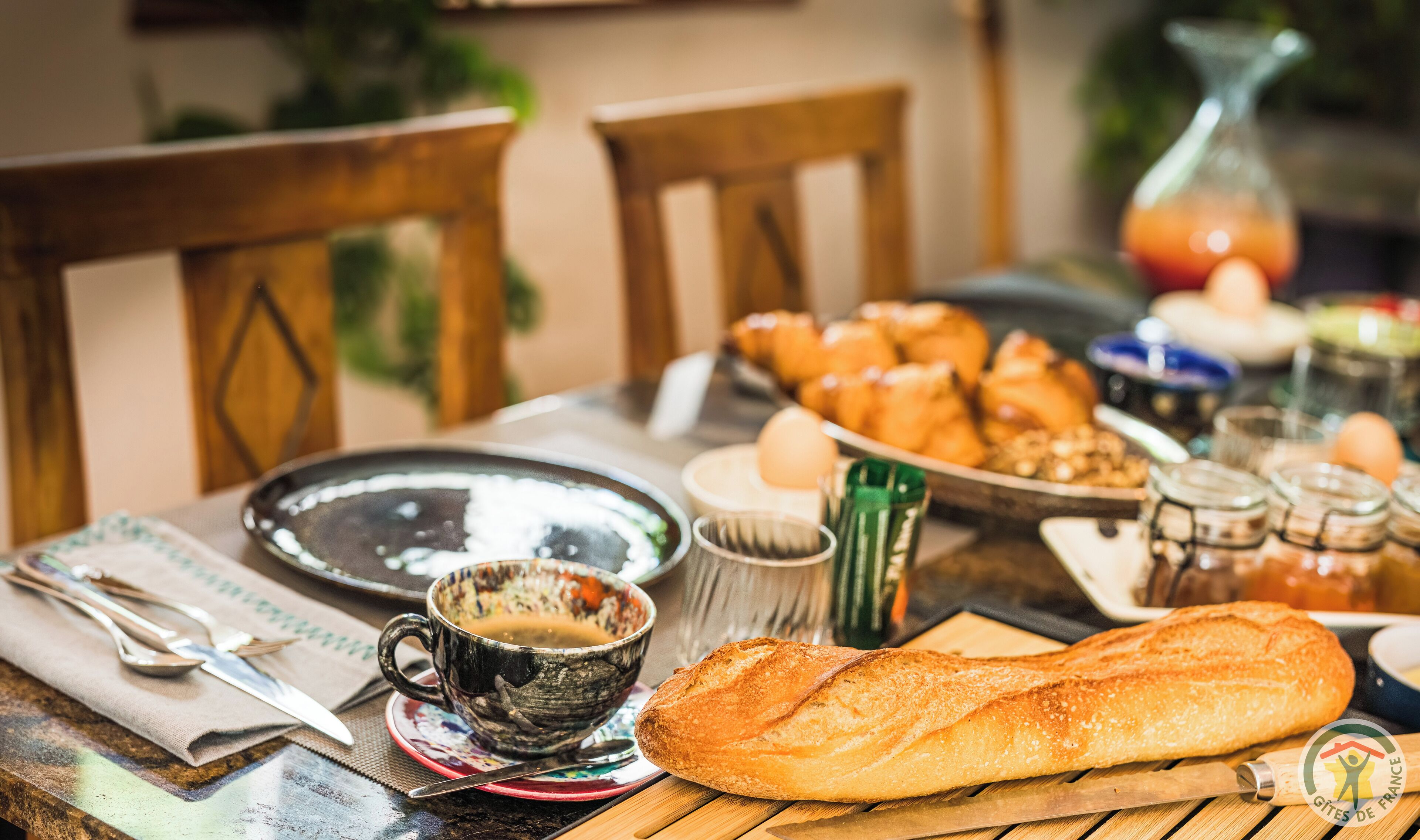 Una mesa de desayuno con un croissant, una baguette, una taza de café y varios condimentos.