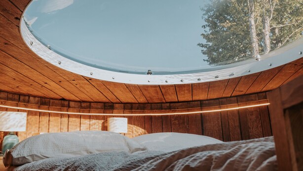 A circular skylight in a wooden room with a bed and a lamp. - Le Nid du Coucou (Cocumont)