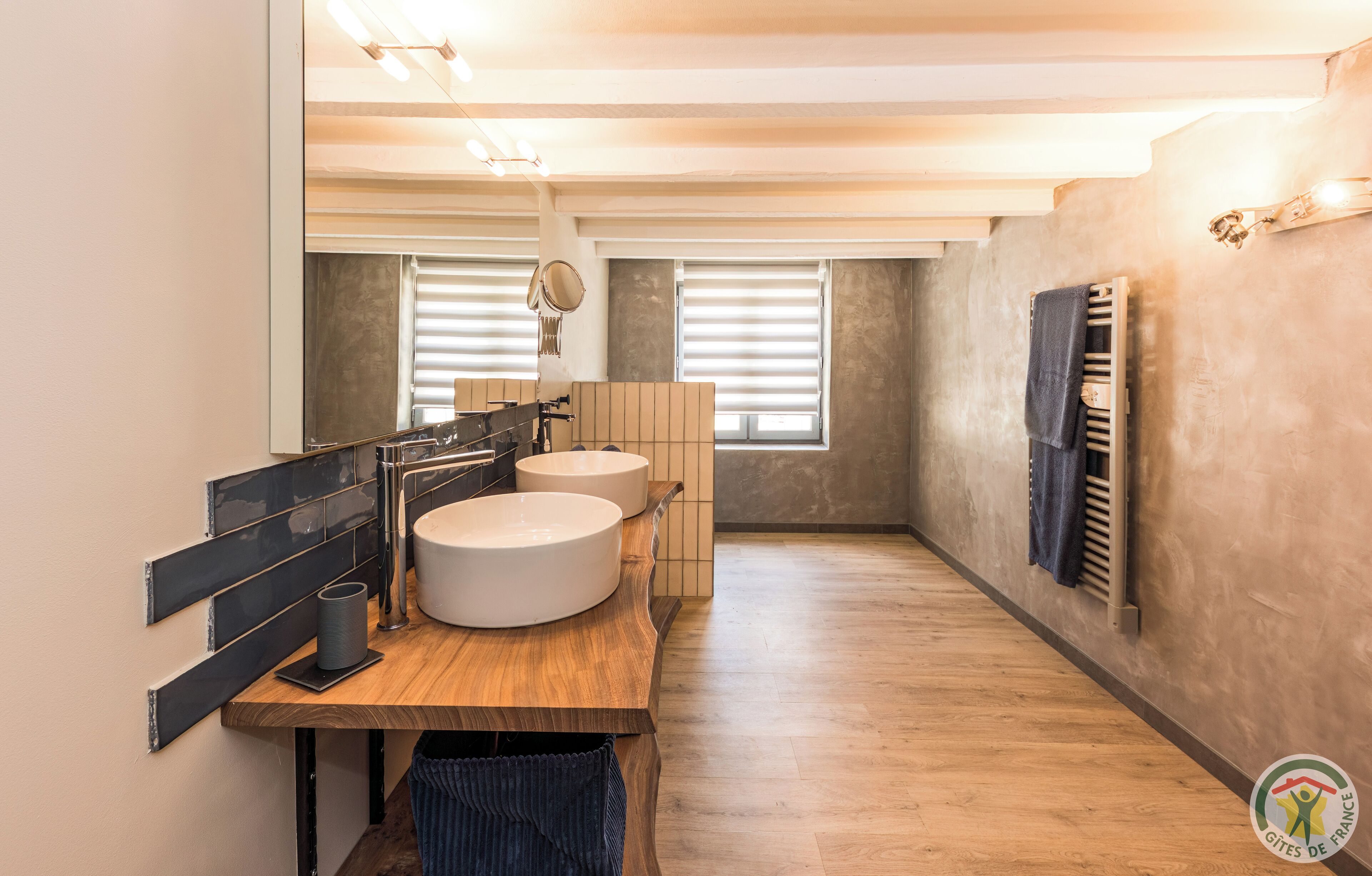 A modern bathroom with two sinks, a wooden vanity, a mirror, and a towel rack.