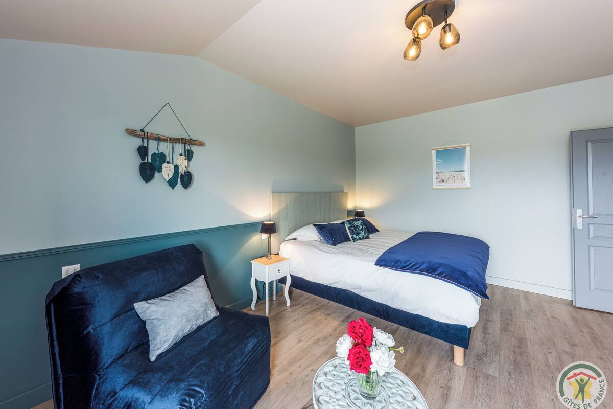 Ein Schlafzimmer mit Bett, Stuhl, Nachttisch, Lampe und Wandbild.