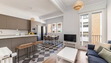 Un apartamento moderno con cocina, comedor y sala de estar. Cuenta con piso de cuadros, un sofá, un televisor y un balcón con vistas a la ciudad.