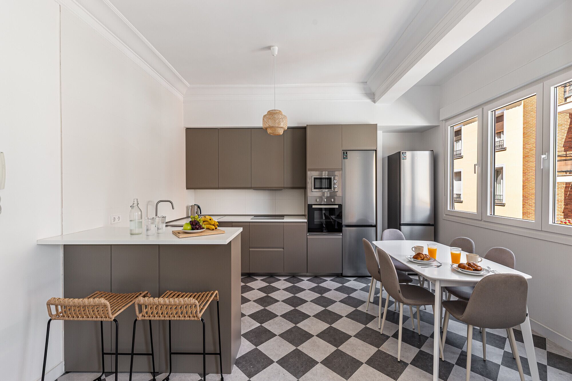 Cocina compacta con comedor, suelo a cuadros, electrodomésticos modernos y vistas a través del ventanal.