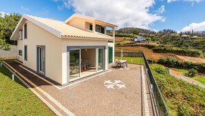 A modern house with a patio, large glass doors, and a view of the surrounding landscape. - Madeiran Vernacular Villa • Sunset Views • Garden • Heating (Ponta do Pargo)