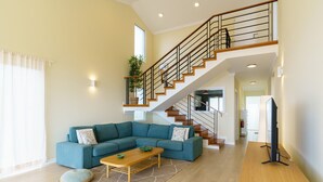A spacious living room with a blue sectional sofa, a wooden coffee table, and a staircase with a wooden railing. - Madeiran Vernacular Villa • Sunset Views • Garden • Heating (Ponta do Pargo)