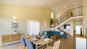 A spacious living area with a dining table set for four, a sofa, and a staircase leading to an upper floor. - Madeiran Vernacular Villa • Sunset Views • Garden • Heating (Ponta do Pargo)