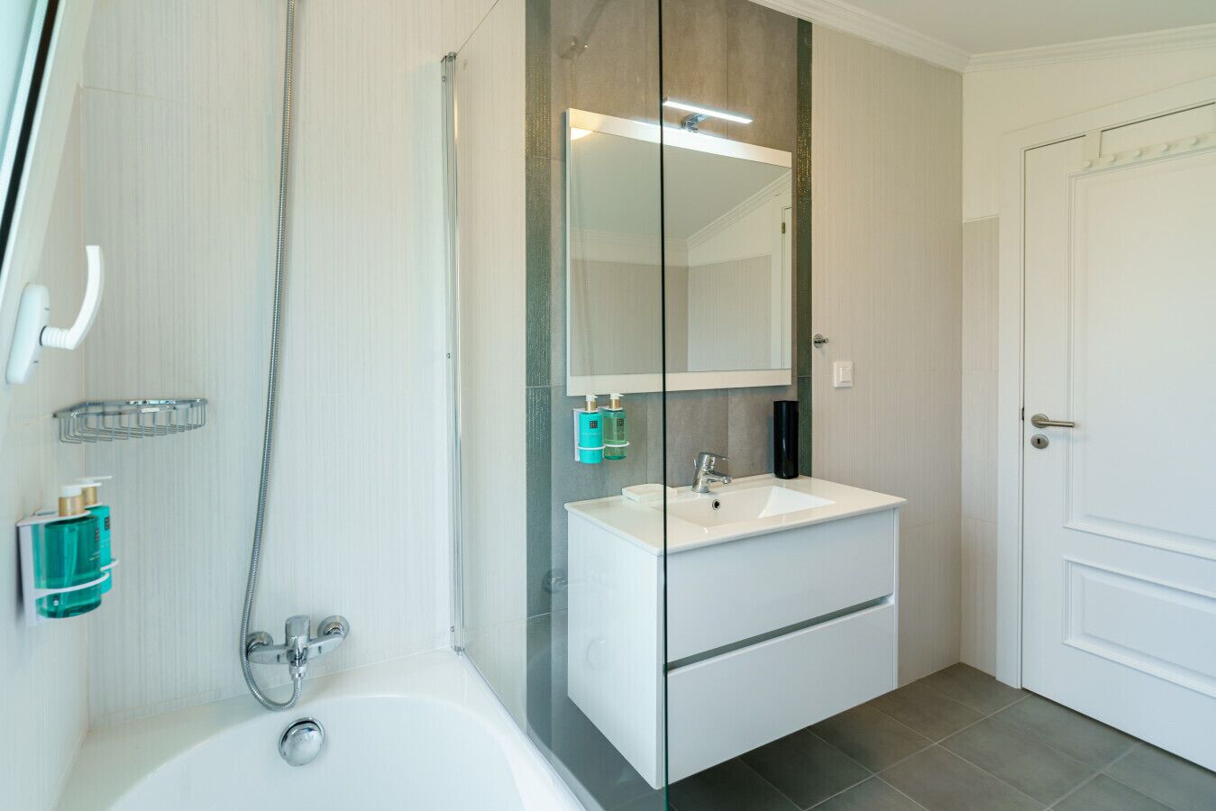 A modern bathroom with a glass-enclosed shower, a white sink with a mirror above, and a door to the right.
