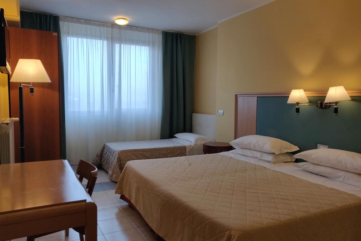Hotellihuone, jossa on kaksi erillistä sänkyä, puinen työpöytä, tuoli ja pöytä.