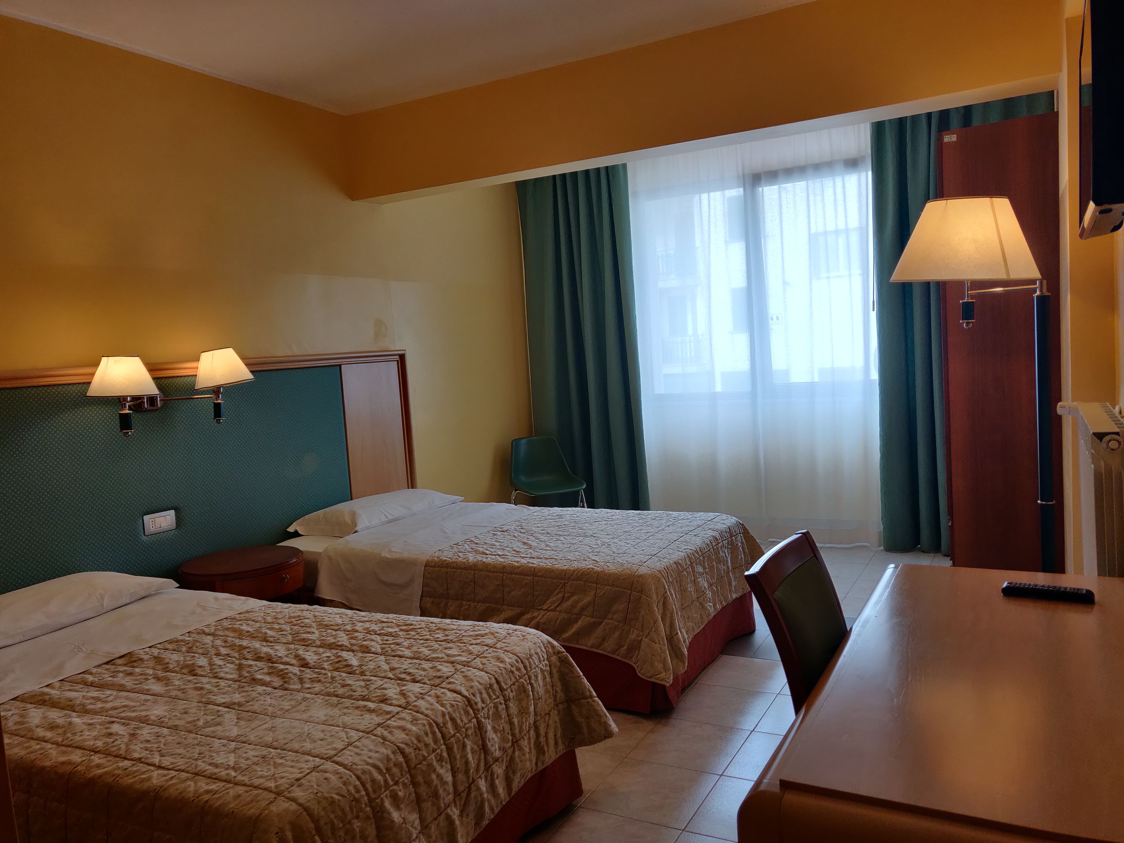 A hotel room with two beds, a desk, a chair, a lamp, and a window with curtains.