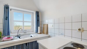 Una cocina con ventana, azulejos blancos, un lavabo y una estufa.