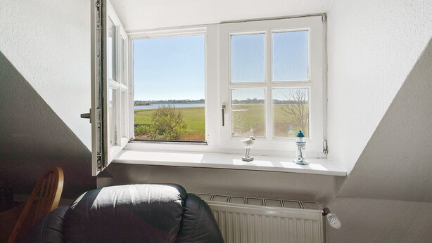 Una habitación con ventana que da a un campo, un radiador y una silla.