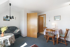 Una habitación con una mesa de comedor, sillas, un sofá, una puerta de madera y una lámpara en el techo.