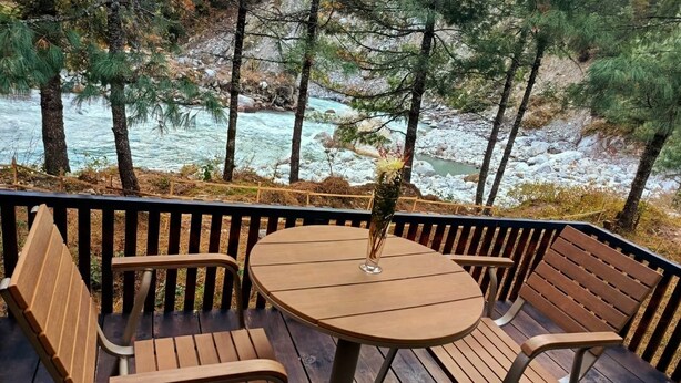 A wooden deck with a round table and benches, overlooking a river and trees. - The Himalayan Phakding (Phakding)