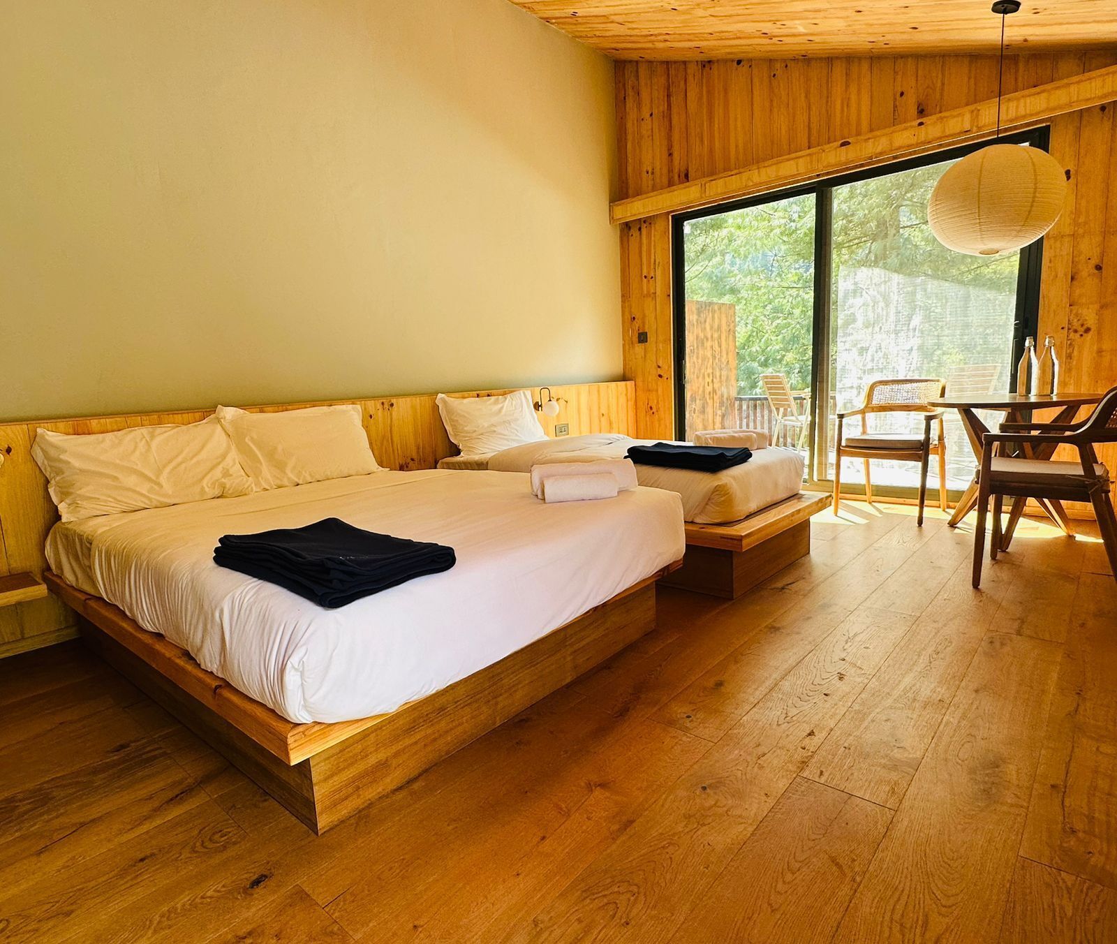Un dormitorio de madera con dos camas, una mesa de comedor y un ventanal grande.