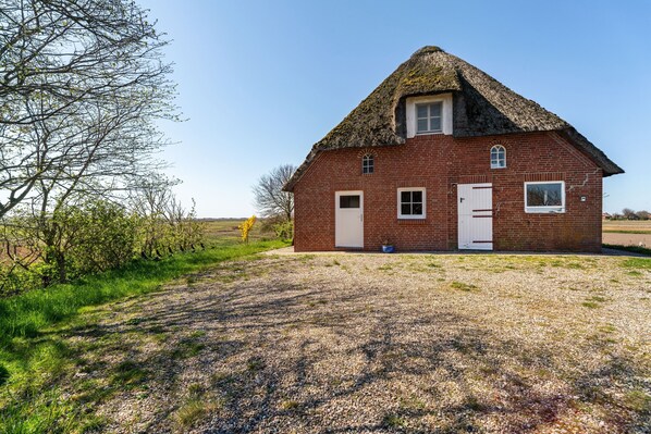 Une maison en briques rouges, avec un toit de chaume, une porte blanche et une petite fenêtre.