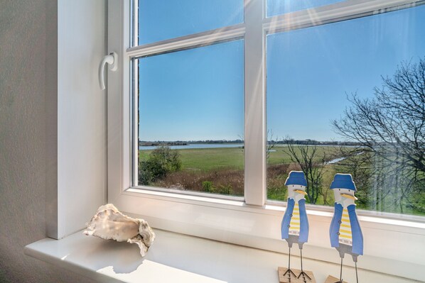 A window with a view of a landscape, a white bench, and two bird figurines.
