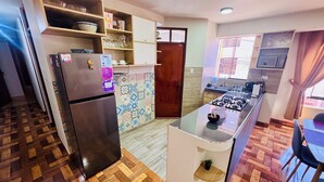 A compact kitchen with a refrigerator, microwave, and gas stove. There is a small island with a sink and a potted plant. The kitchen has wooden flooring and a tiled backsplash. - Comfort in the heart of downtown Tacna (Tacna)